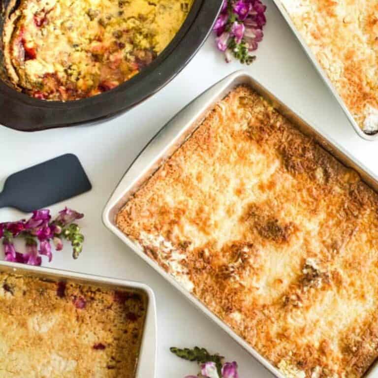 A few baking pans holding variations of dump cakes on a table with flowers and spatulas.
