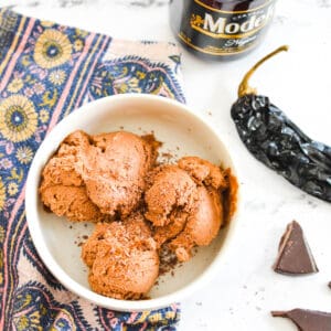 A bowl of chocolate ice cream that is infused with beer and chles with a napkin, a bottle of beer and a chile next to it.