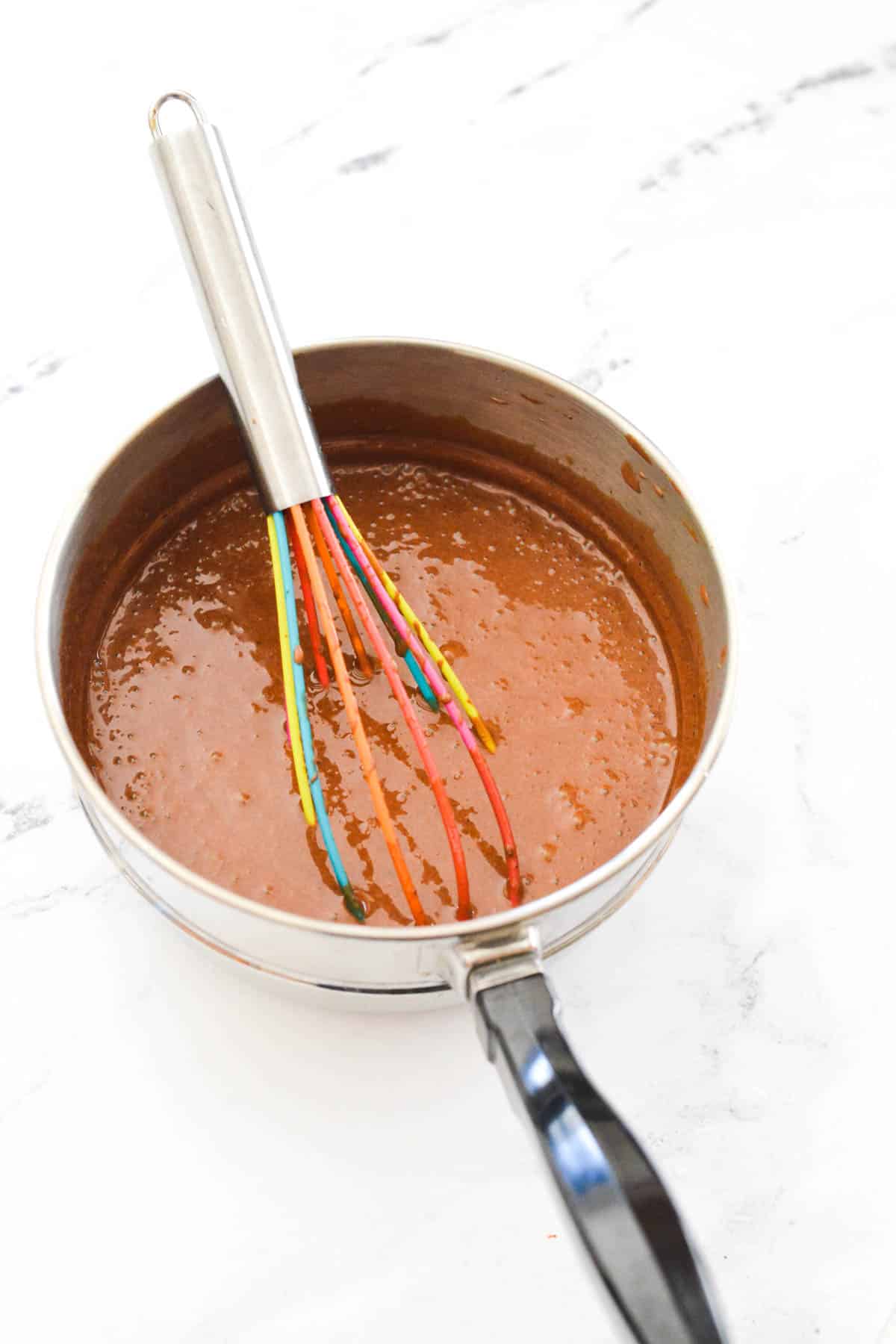 A saucepan with melted chocolate and a whisk.