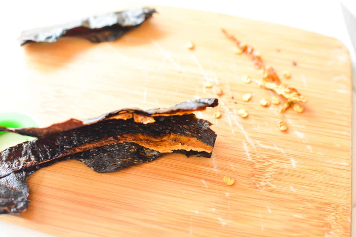 Dried chile on a wooden cutting board with seeds scraped out.