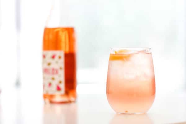 Rose Lemonade Spritzer in glass with a bottle of rosé in the background. 
