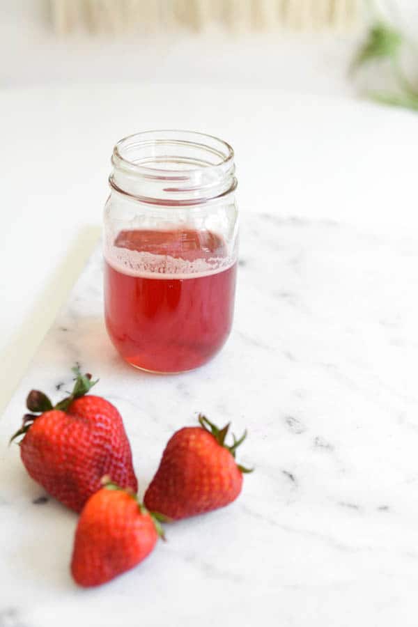 Strawberry syrup in mason jar on a cutting board next to fresh strawberries.