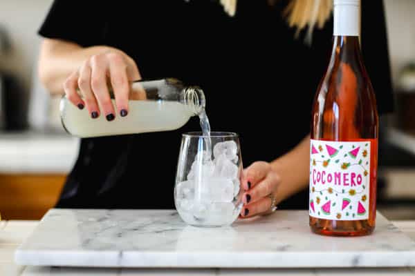 Woman pouring lemonade into a glass next to a bottle of rosé.