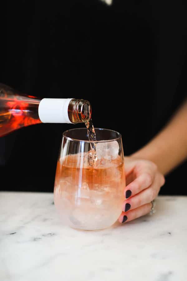 Woman pouring rose on top of lemonade in a stemless wine glass.