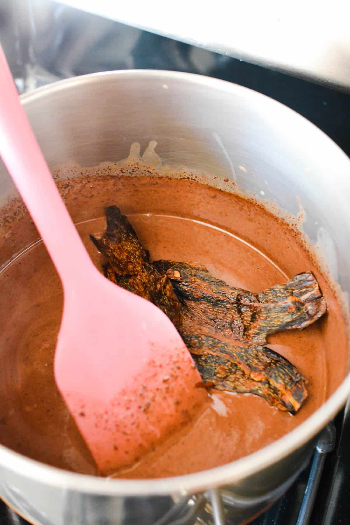 A sauce pan with melted chocolate with dried chiles in it to infuse it.