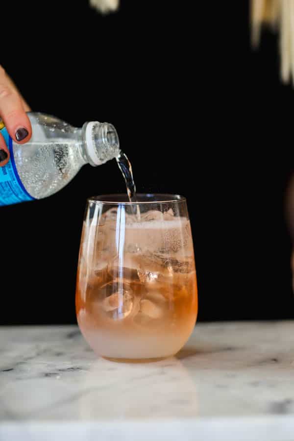 Pouring club soda into rosé wine and lemonade in a stemless wine glass.