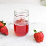 Strawberry Simple syrup in mason jar with fresh strawberries on a cutting board.