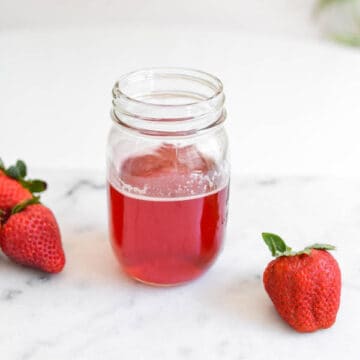 Strawberry Simple syrup in mason jar with fresh strawberries on a cutting board.