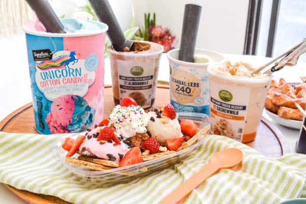 A bowl holding an ice cream nachos sundae with ice cream containers in the background.