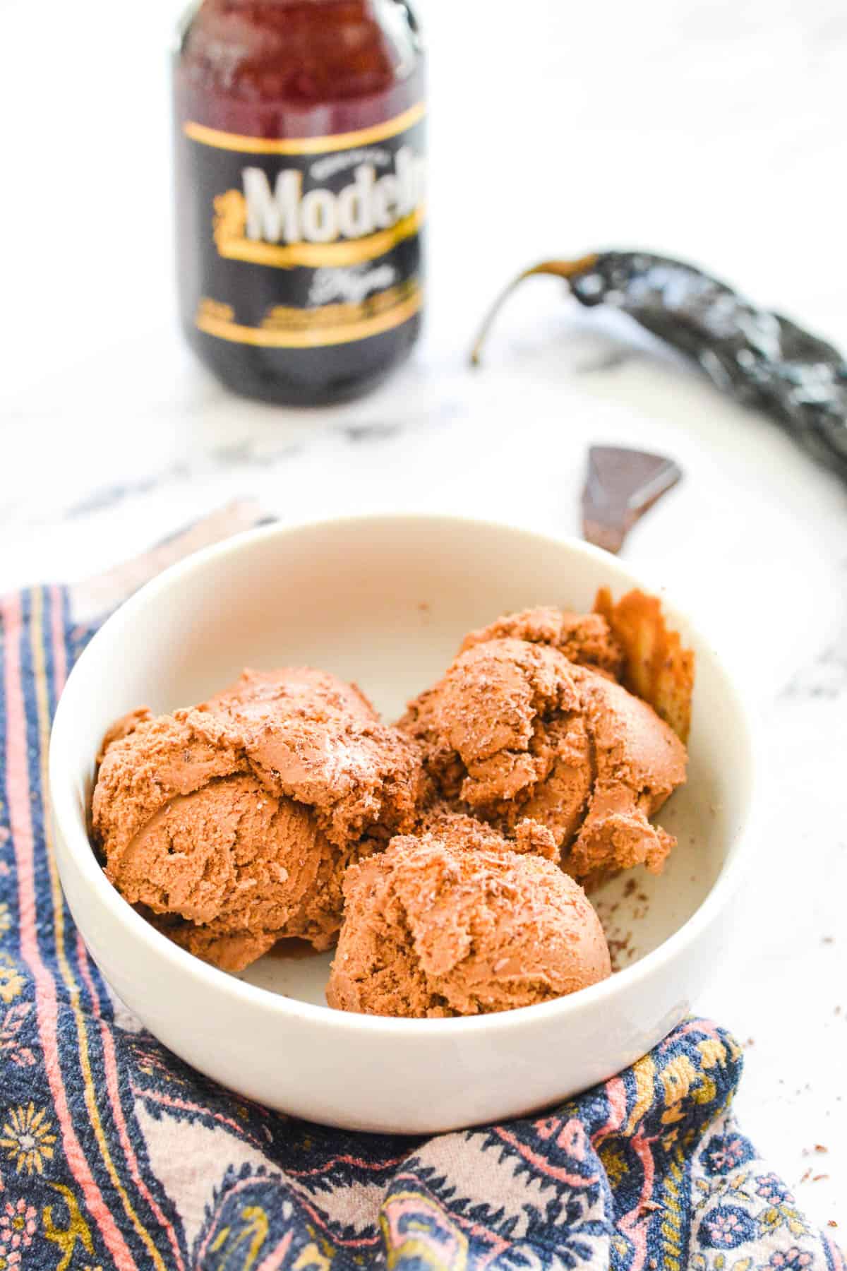 A bowl holding scoops of chocolate ice cream with a bottle of beer in the background.