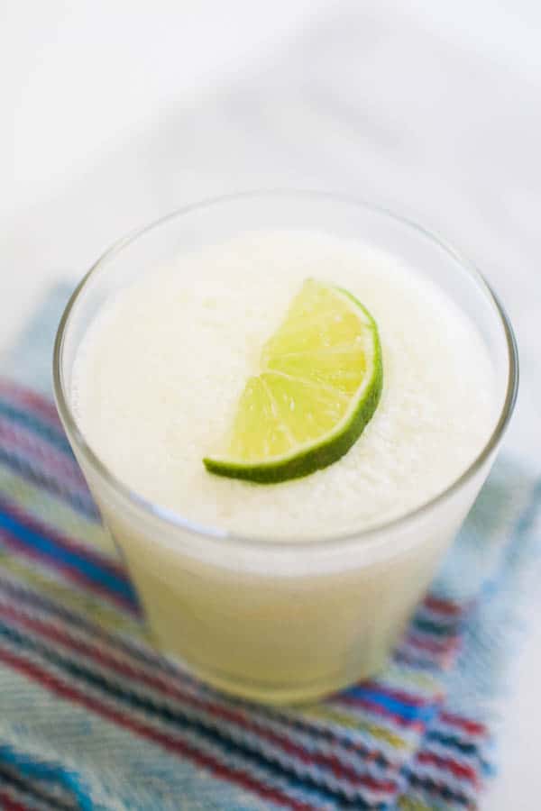 Easy frozen margarita recipe in a glass with a lime wedge garnish. 