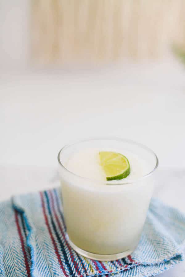 A glass of frozen limeade margarita on a table with a lime slice on top.