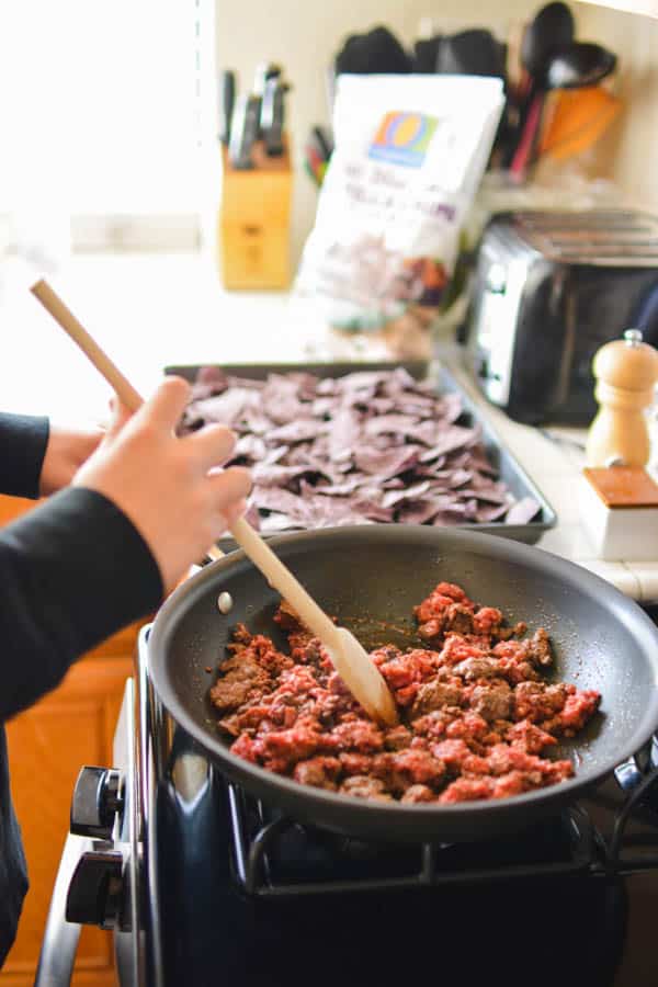 Boy cooking ground taco meat on the stove top.