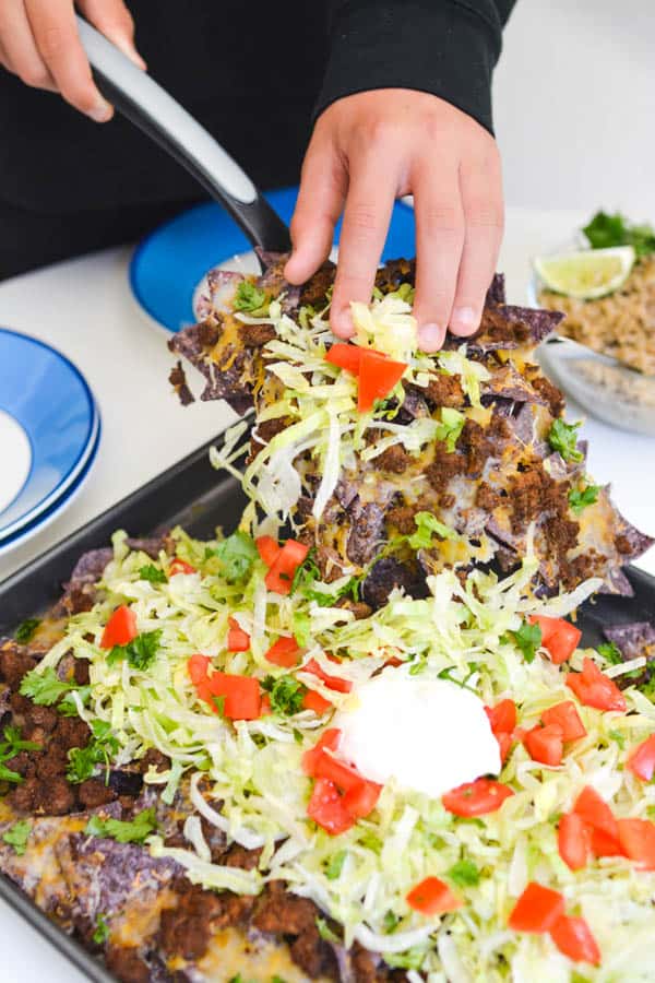 Boy using spatula to take a serving of loaded nachos.