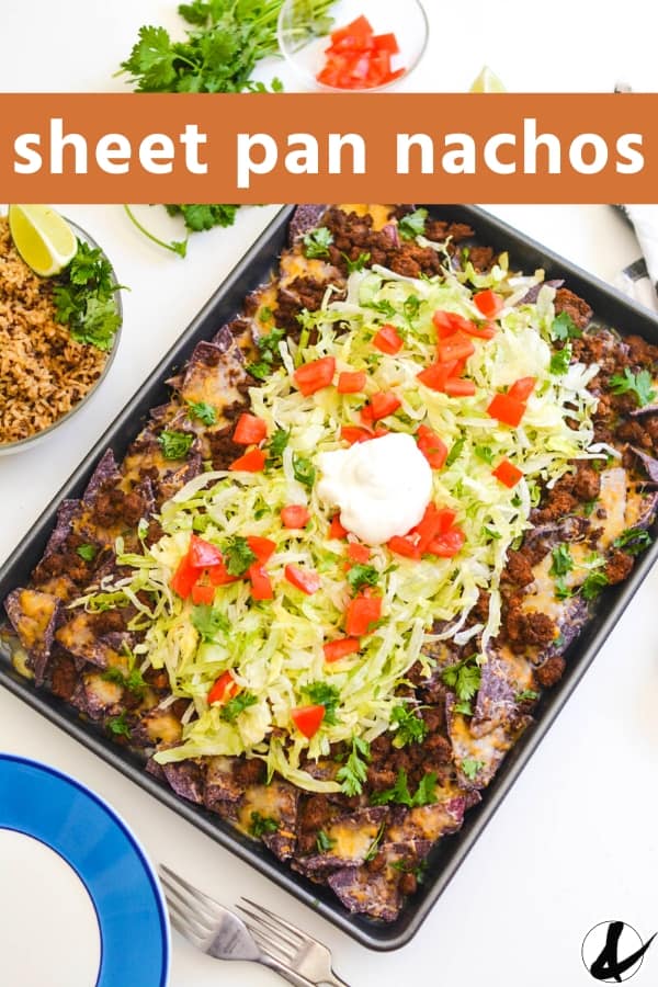 Loaded sheet pan nachos with shredded lettuce and toppings on a table.
