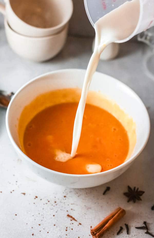 Cream being poured into a bowl with ingredients to make a Fireball Pumpkin Pie. 