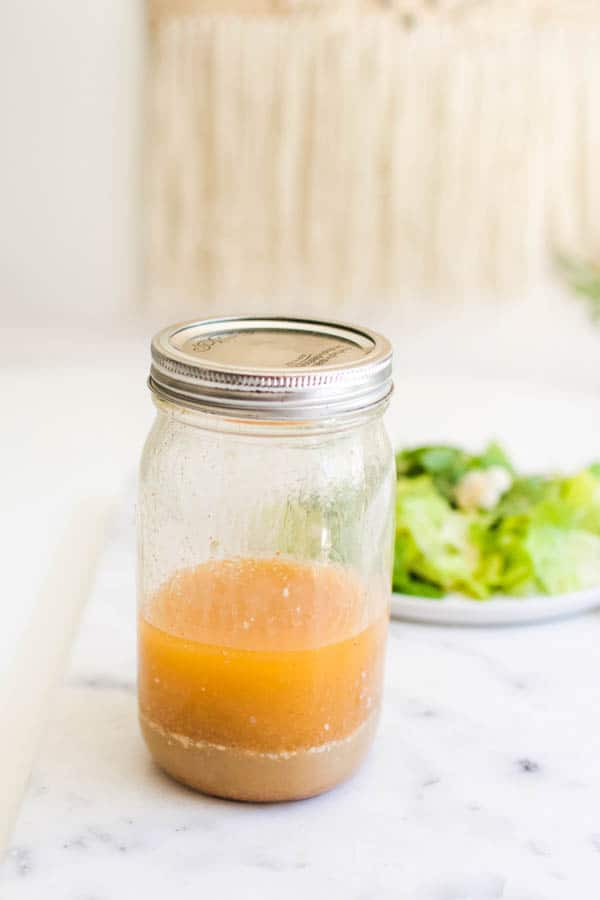 Jar of Blue Cheese Vinaigrette on a cutting board next to a romaine salad.