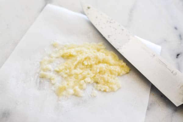 Garlic and salt paste on a cutting board by a knife.