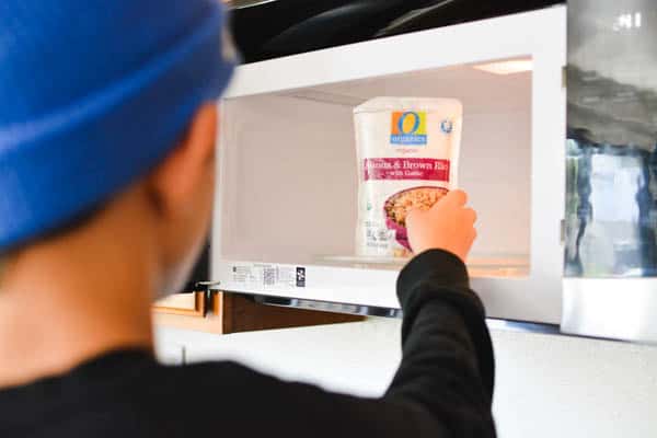 Boy putting a microwavable brown rice and quinoa side dish into the microwave.