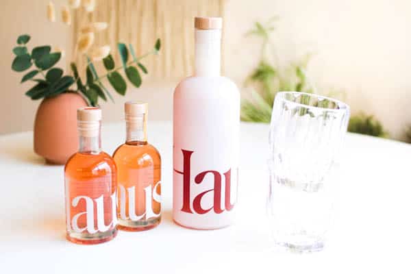 Haus aperitif bottles on a table next to some glasses.