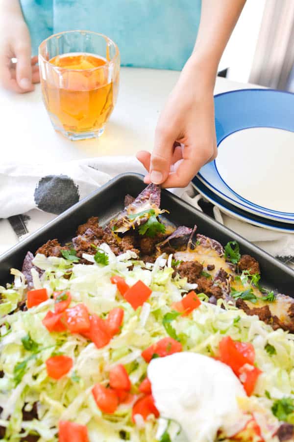 Kid grabbing a chip off of sheet pan nachos.