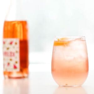 A stemless wine glass filled with rosé and lemonade in front of a wine bottle.