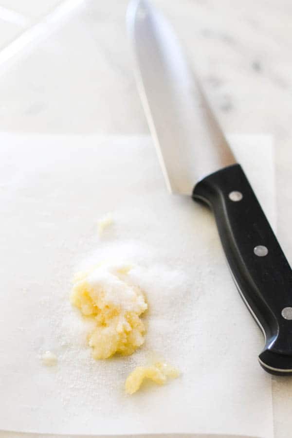 Salt and crushed garlic on a cutting board next to a knife.