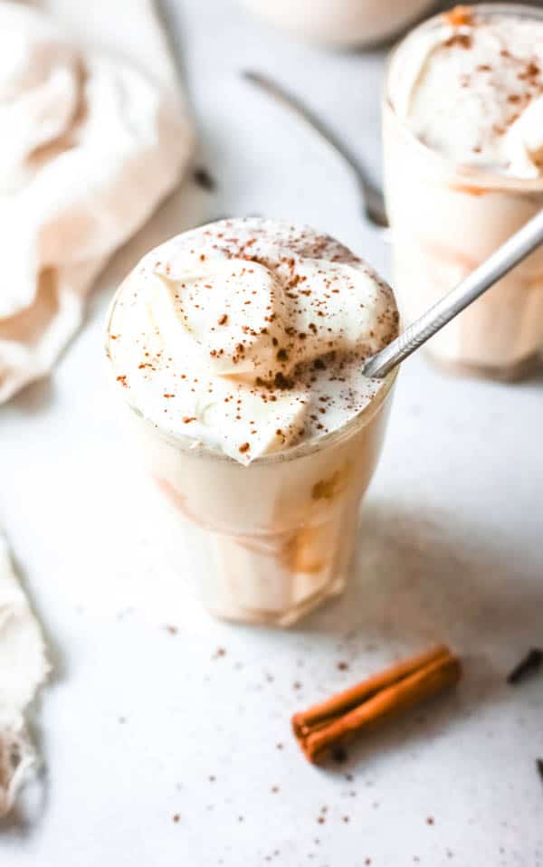 Pumpkin pie milkshake with salted caramel in a glass topped with whipped cream and cinnamon.