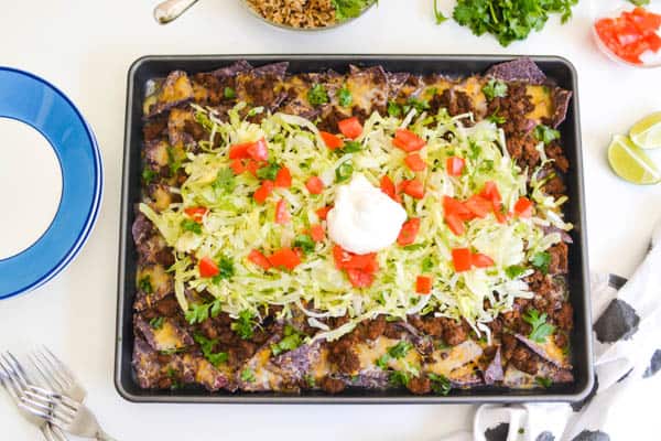 Sheet pan nachos with lettuce, tomatoes and sour cream on top.