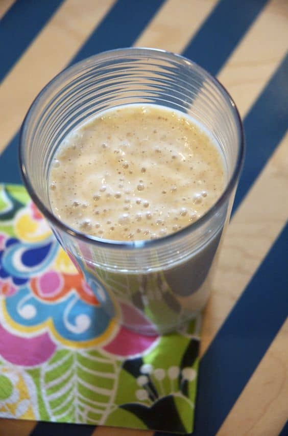 Banana oatmeal smoothie in a ringed glass on a blue striped tray with a colorful napkin.