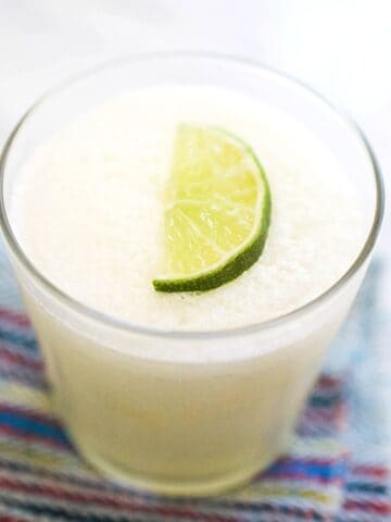 Close up of a frozen margarita in a cocktail glass on a table with a lime wedge garnish.