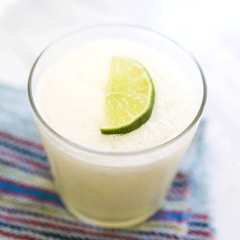 Close up of a frozen margarita in a cocktail glass on a table with a lime wedge garnish.