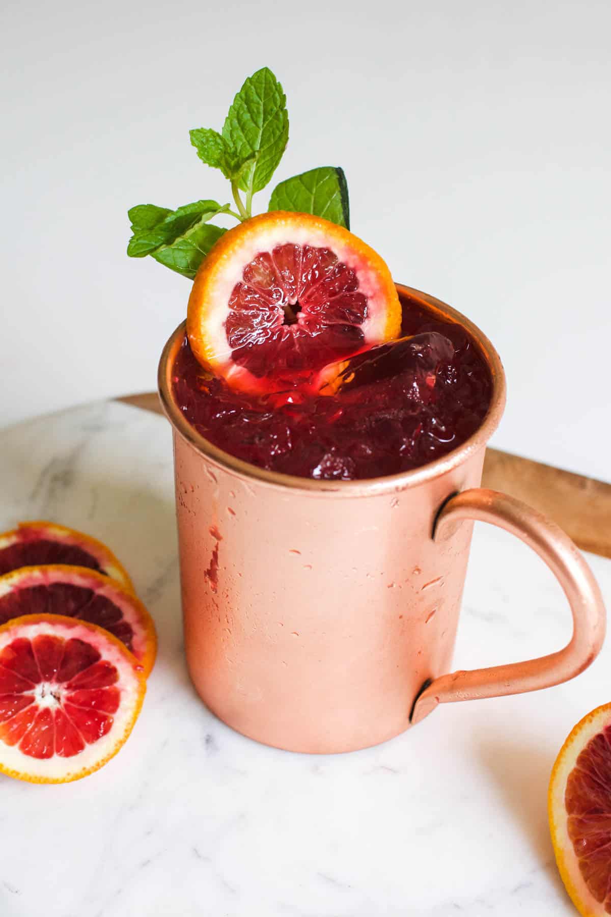 Close up of a copper mug with a cocktail topped with fresh mint and blood orange slices.