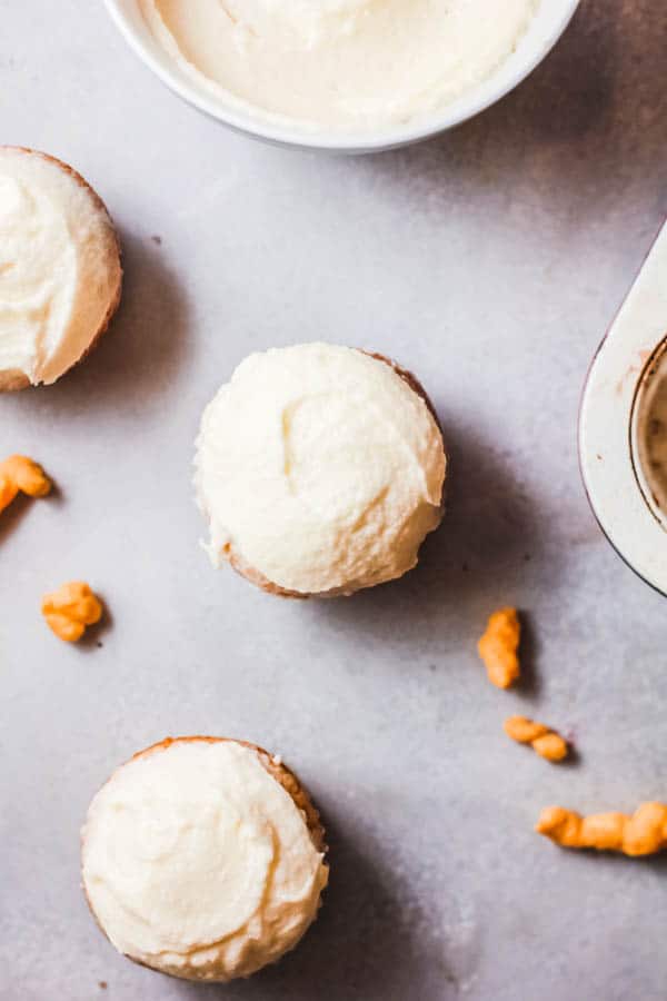 Frosted cupcakes on a table with Cheetos scattered around. 