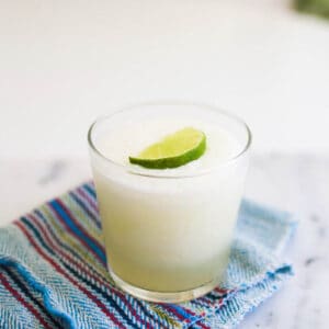 A frozen margarita in a glass with a lime slice on top.