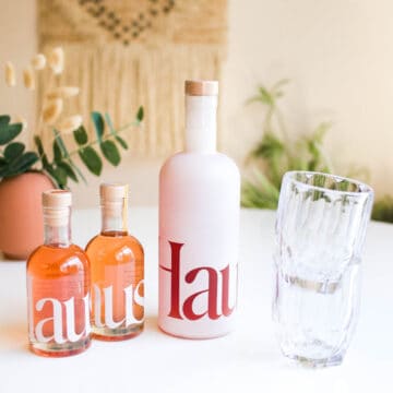 A few bottles of Haus on a table next to some stacked glasses.