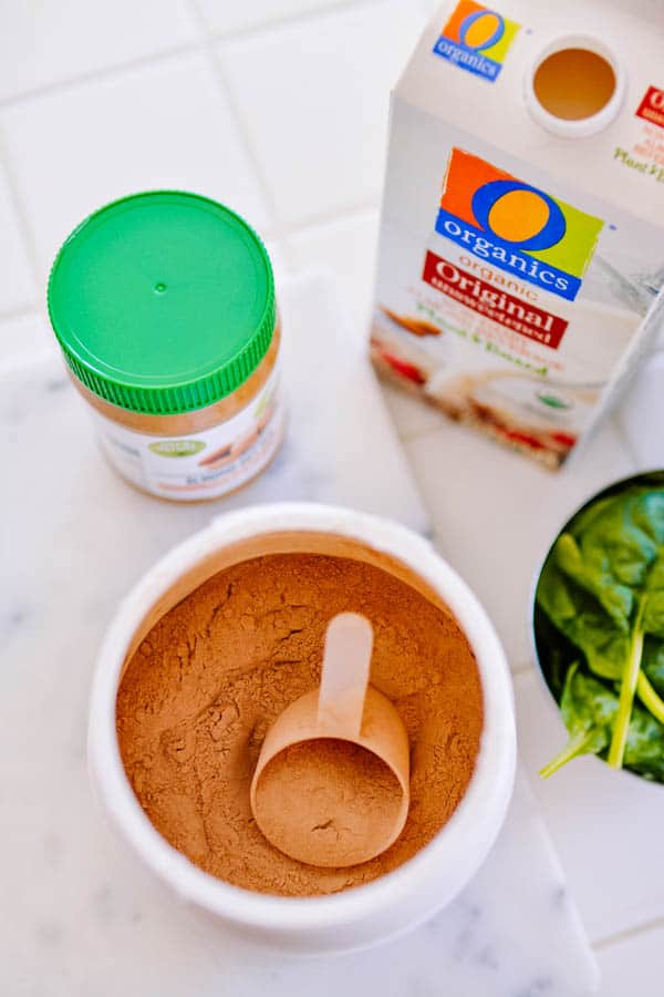 A top down view of an open chocolate protein powder container next to other ingredients for a smoothie.