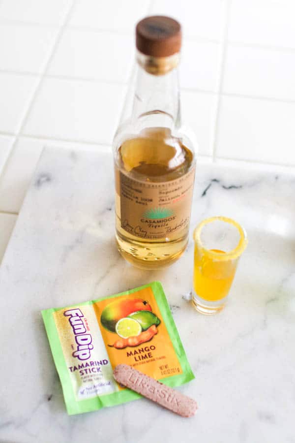 A bottle of tequila on a cutting board next to Fun Dip candy and a small shot.