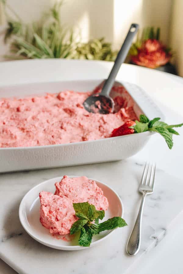 Easy pink strawberry JELLO dessert in a baking dish with a serving on a plate next to it.