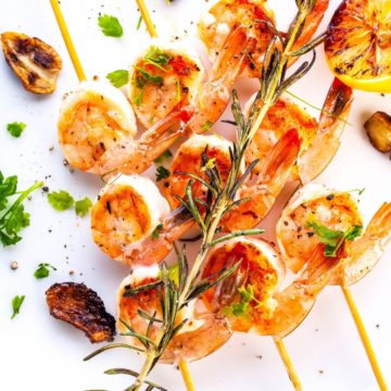 Three grilled garlic shrimp skewers with a white wine spritz and fresh rosemary.