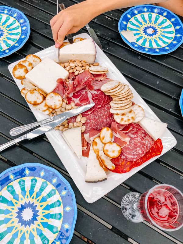 Charcuterie board on a table next to patterned plates.