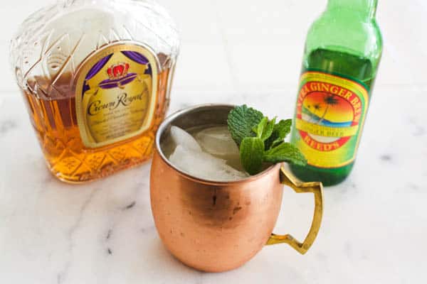 A whiskey mule on a table in a copper mug next to a bottle of whiskey and ginger beer.