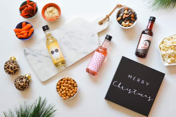 Mini bottles of wine laying on a table with snacks and a Merry Christmas sign around it. 