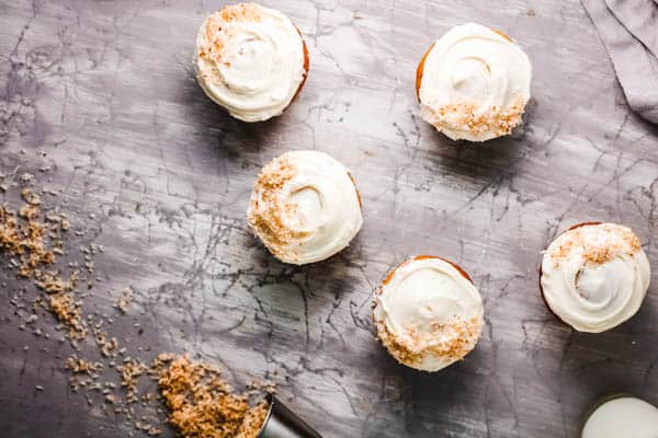 Several frosted coconut cupcakes that have been infused with Rum on a table.