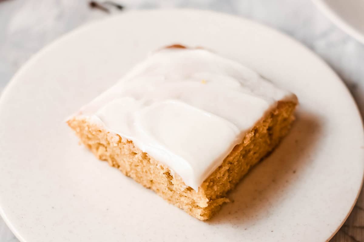 A square piece of pumpkin sheet cake with cream cheese frosting on a white dessert plate.
