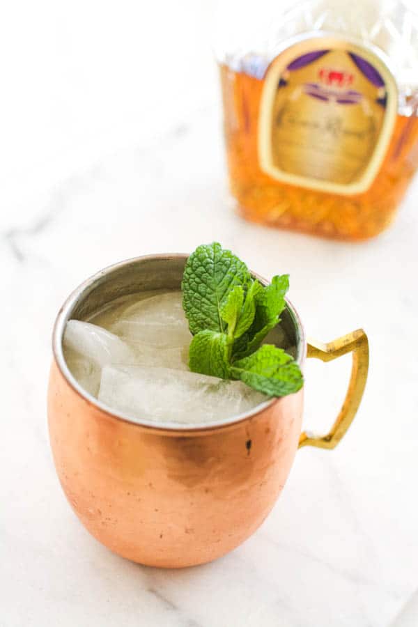 Copper mug holding a Moscow Mule with whiskey next to a bottle of Crown Royale.