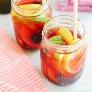 Two jars with sliced fruit and hibiscus tea sangria with a straw.
