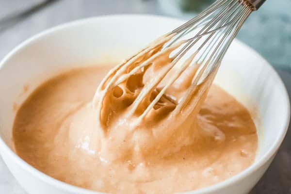 Mixing bowl with pumpkin cake batter with a whisk sitting in it.