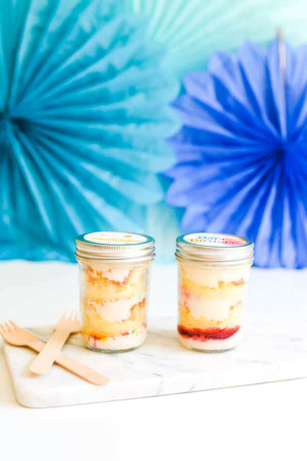 2 jars with cupcakes on a table in front of party decorations.