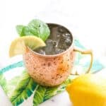 Lemonade mule on top of a tropical patterned napkin with a whole lemon to the side.